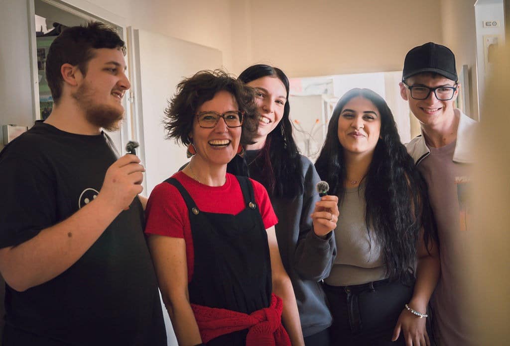 Ein Gruppenfoto von den Bigsteilnehmer*innen mit der Ausbildnerin. Zwei Personen halten Mikrofone und wirken wie bei einer Präsentation.