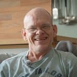 Person sitzt auf einem Sofa und lacht offen in die Kamera.