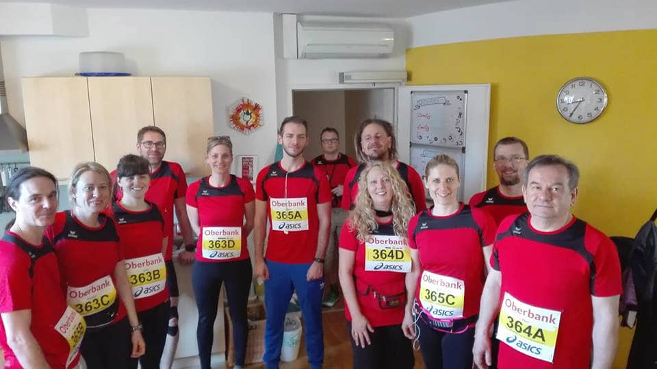 Eine Gruppe strahlender Mitarbeiter in Roten Lauftshirt und Laufnummern an der Brust. Bereit für den Marathon.