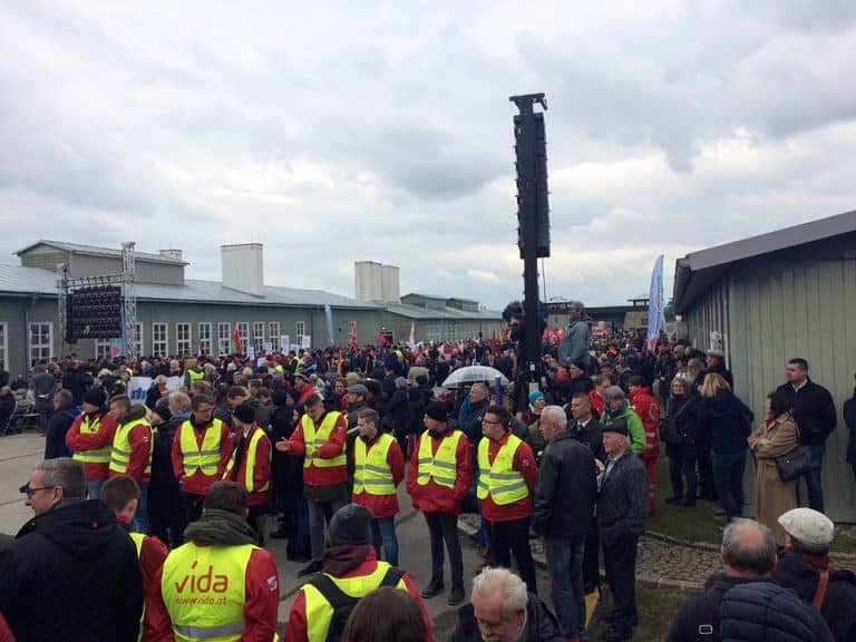 Eine Demonstration im KZ Mauthausen. Eine Gruppe Männer Steht mit einer Warnweste herum.
