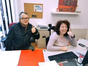 Thomas und Lydia die zusammen am Schreibtisch sitzen und in die Kamera den Daumen zeigen.