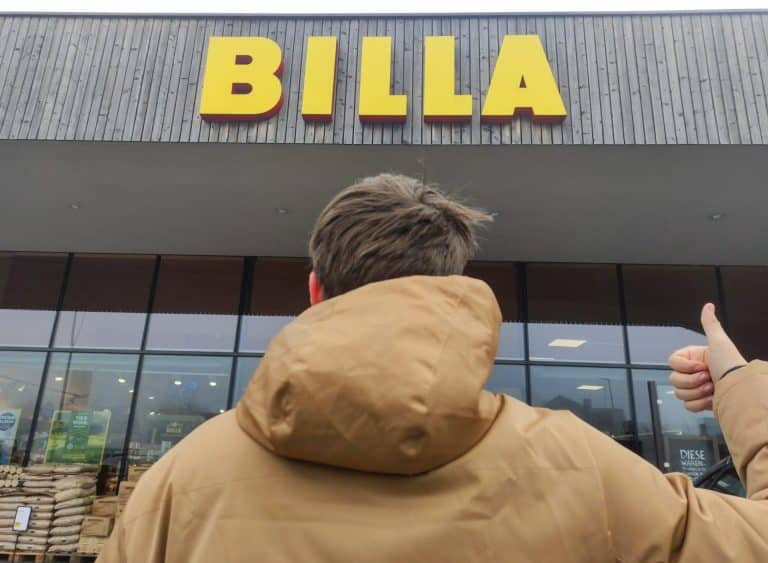 Ein Bild von einem AFit Teilnehmer der mit dem Daumen Zeigend vor einem Billa-Lebensmittelmarkt steht.