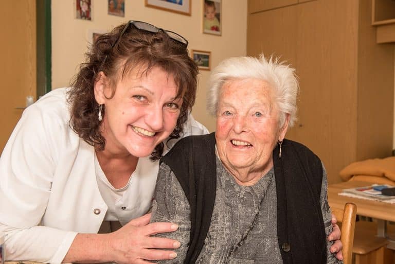 Ein Foto von eine Älteren Dame und einer Kollegin die gemeinsam in die Kamera grinsen.