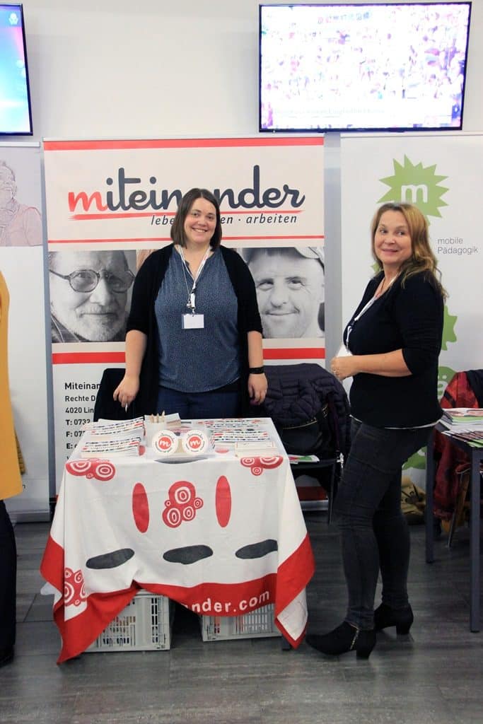 Ein Foto von dem Messestand auf der Connect in Linz. Am Tisch sieht man die Broschüren und Karten zum mitnehmen.
