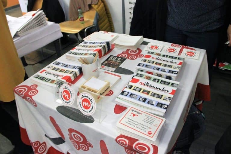 Ein Foto von dem Messestand auf der Connect in Linz. Am Tisch sieht man die Broschüren und Karten zum mitnehmen.