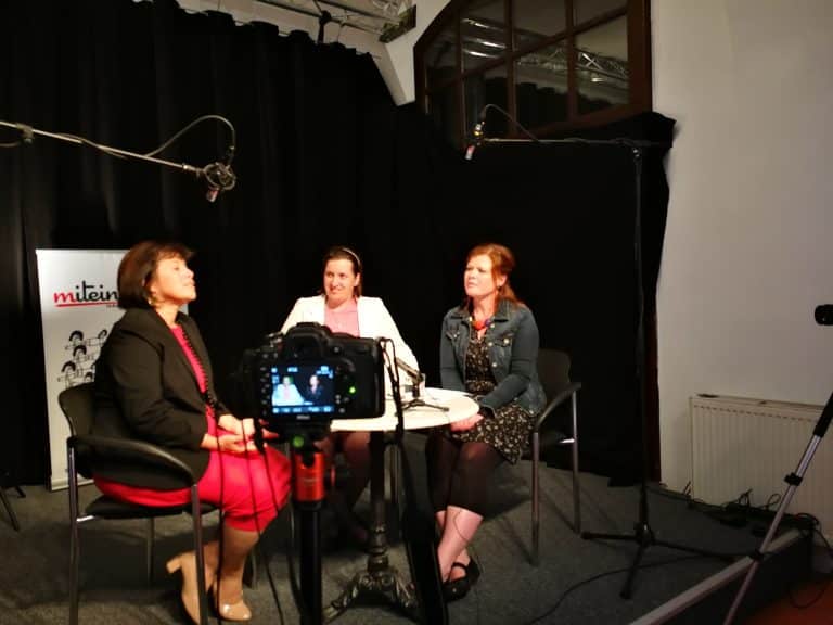 Eine Szene von dem Interview mit Birgit Gerstorfer. Drei Personen sitzen bei einem Marmor-Tisch umgeben von 2 Kameras und 2 Mikrofonen.