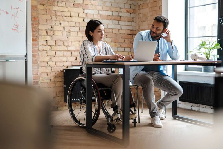 Zwei Personen sitzen am Tisch und unterhalten sich neben einen Laptop.