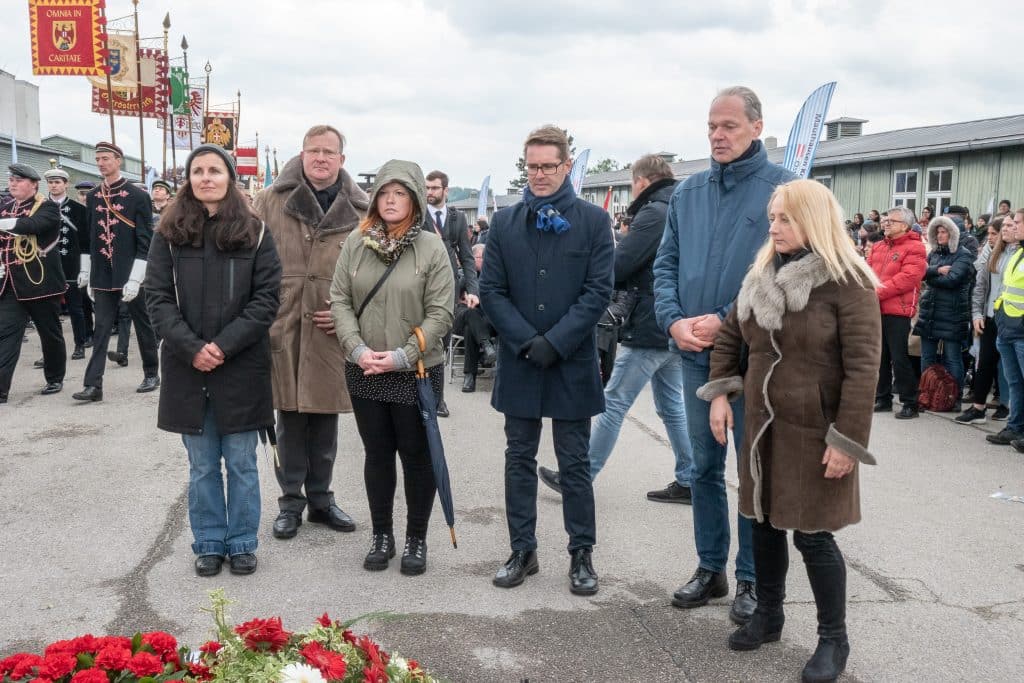 Eine Gruppe Personen steht um den Blumen und gedenkt den Todesopfer aus der NS Zeit.